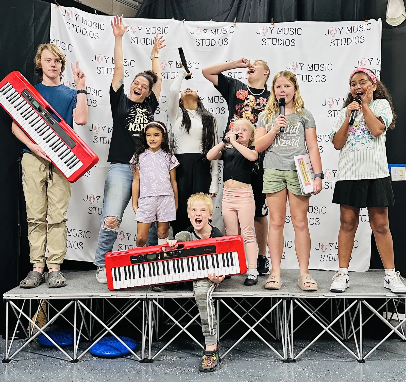 Kids performing on stage with microphones and a keytar at a studio showcase